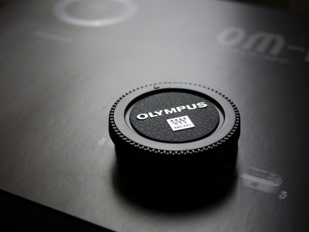 Detailed close-up of an Olympus camera lens cap on a dark surface, showcasing texture and branding.